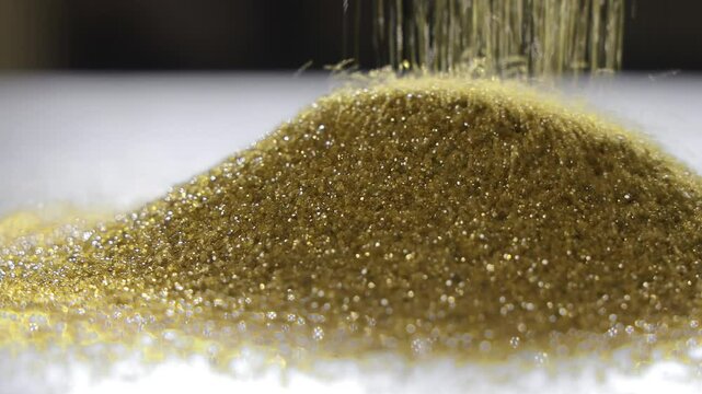 Golden abrasive particles falling into pile, Close-up view of industrial material used in sandblasting or filtration processes