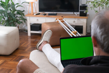 Injured senior man using laptop with green screen at home