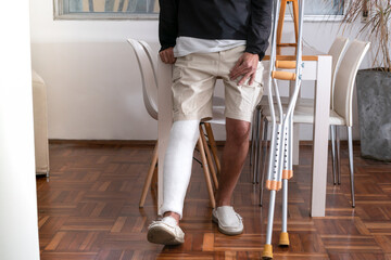 Man leaning on table with broken leg and crutches at home