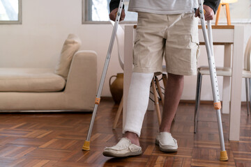 Man walking with crutches and broken leg in cast at home