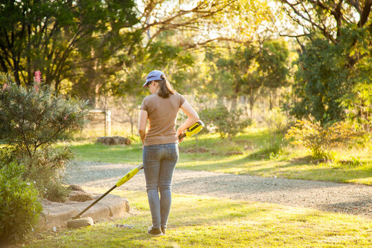 Teen girl cutting grass with whipper snipper in golden afternoon light