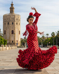 Fototapeta premium Graceful flamenco dancer in a red polka dot dress performing near Seville Torre del Oro, showcasing Andalusian culture and tradition.