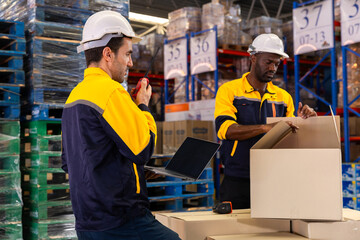 Warehouse technician kneels beside pallet to scan boxes with handheld scanner, checking barcodes...