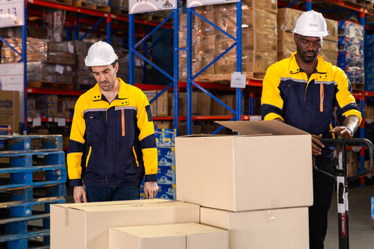 Warehouse technician kneels beside pallet to scan boxes with handheld scanner, checking barcodes before dispatch on busy distribution floor lined with reusable pallets. African male, efficiency worker