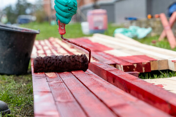 Construction worker applying red paint on wooden planks with roller brush