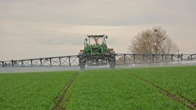 Self-propelled sprayer moving forward across crop field, Agricultural machinery spraying fertilizer over young green plants