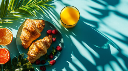 Continental breakfast on a vibrant blue table with shadows from tropical plants, croissants, berries, and juice