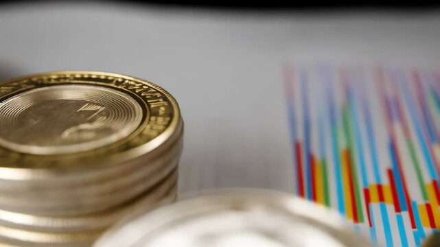 Stacks of gold and silver coins representing growth and investment on top of a colorful business chart with up and down lines showing financial trends.