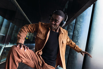 Stylish dancer wearing headphones is enjoying music and dancing in a modern building