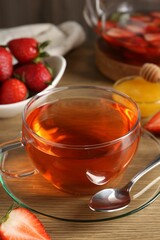 Aromatic fruit tea with strawberries and honey on wooden table, closeup