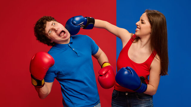 Dramatic young man and woman, couple wearing boxing gloves and acting out a punch to the face, with exaggerated expressions against vivid red and blue background. Concept of humor, sport, reaction.