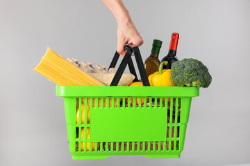 Fototapeta premium Man holding shopping basket with different products on grey background, closeup