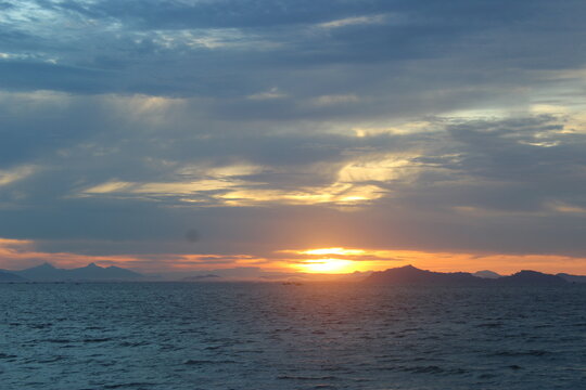 Vibrant sunset horizon. The sun dips below the horizon, casting a warm glow over the calm ocean and rocky shore