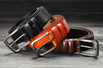 Three leather belts on wooden table, closeup