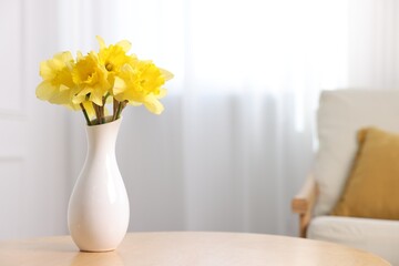 Beautiful daffodils in vase on wooden table at home. Space for text