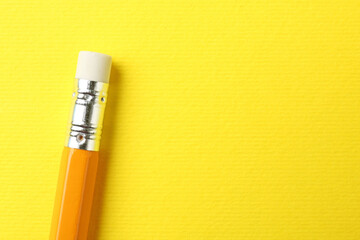 One pencil with eraser on yellow background, top view. Space for text