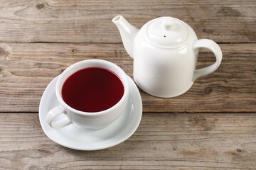 Delicious hibiscus tea in cup and teapot on wooden table