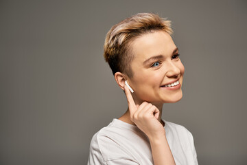 Joyful young woman celebrates confidence with a smile and modern earbuds in a simple setting