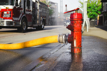 Close up of fire hydrant with hose attached and defocused fire truck. Supply line or hydrant line...