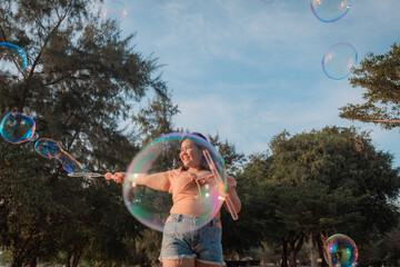 Joyful young chubby woman is playing with bubbles outdoor park setting captured mid-laughter...