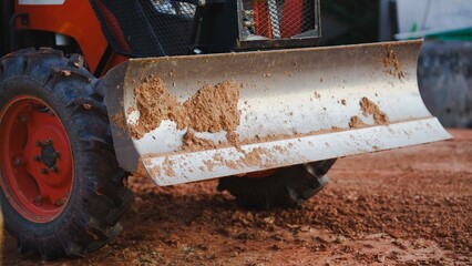A close-up of a metal blade attached to a tractor, showing dirt and wear from use.