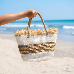  Hand holding two-tone woven straw beach bag with fringe detail