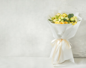  bouquet of pale yellow peony-style roses wrapped in white paper with satin ribbon gray background with putty effect. banner. Elegant floral gift for weddings, birthdays, or special occasions.
