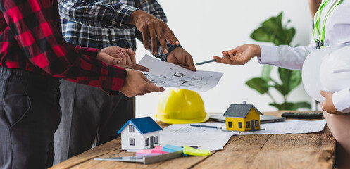 Architect discussing housing project with blueprints and miniature house. Architects gather in office, examining blueprint house, teamwork in real estate project planning.