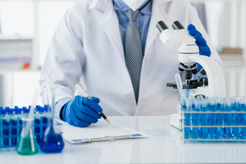 Fototapeta premium Scientist taking notes during experiment in laboratory. The lab table is filled with test tubes, beakers, and a microscope.