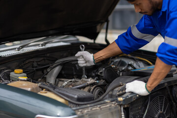Auto mechanic repairing engine using wrench in garage. Mechanic in a jumpsuit fixes a car engine in a garage workshop.