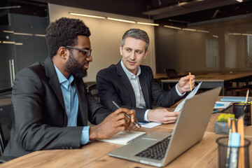 Two businessmen sitting in the office at the laptop and working on the project