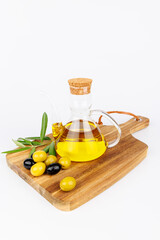 Top view of olive oil bottle, green olives and olive twigs on dark cutting board with white background