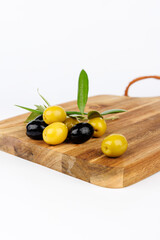 Mixed olives and olive branches displayed on dark wood board against white background