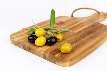 Green and black olives with olive branches on a dark cutting board over white background