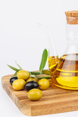 Bottle of olive oil with green olives and olive branches on wooden board, displayed on clean white...