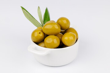 White bowl with green olives and olive branch on clean white background