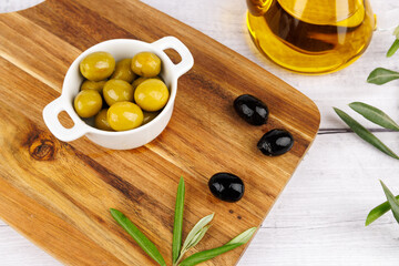 Mediterranean olive oil still life with green olives, black olives, and olive leaves on wood board