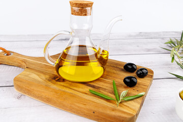 Olive oil still life with rustic cutting board, olives, and olive twigs on white background