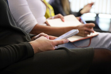 Smartphone in female hands, women with mobile phones and writing pads sitting indoors on a public event