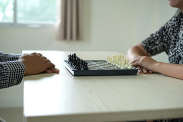 Two young asian business couple are playing chess at home, young man holds a chess to determine...