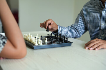 Two young asian business couple are playing chess at home, young man holds a chess to determine...