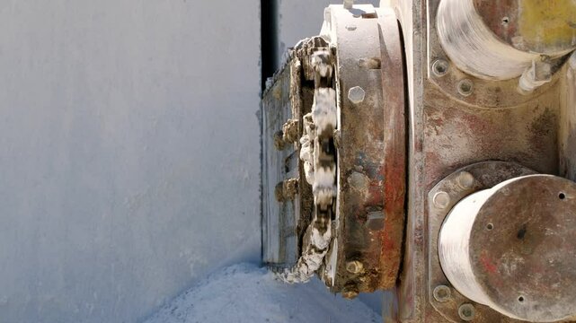 Industrial chainsaw cutting white marble block during extraction at rugged rocky quarry with dramatic stone cutting process