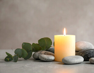 A glowing candle surrounded by smooth stones and fresh eucalyptus leaves on a table.