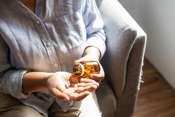 An elderly Thai woman is pouring medicine from a bottle and preparing to take it