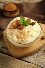 Delicious rice pudding with cinnamon, almonds and mint on wooden table, closeup
