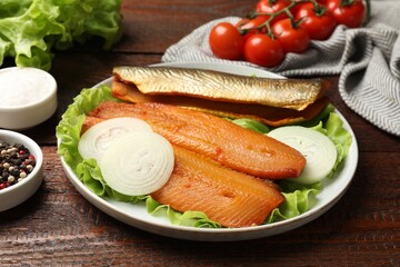 Delicious smoked herring fillets with onions and lettuce on wooden table, closeup
