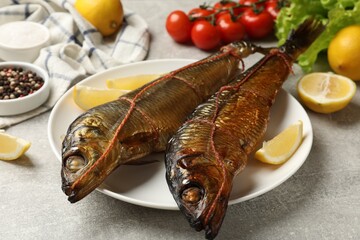 Delicious smoked herrings with lemon slices and other products on grey table, closeup
