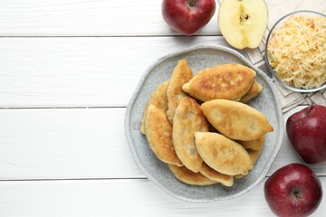Delicious fried pyrizhky (stuffed pies) and apples on white wooden table, flat lay. Space for text