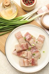 Pieces of delicious herring with green onions on light table, flat lay