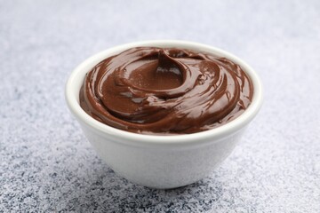 Delicious chocolate pudding in bowl on light grey textured table, closeup